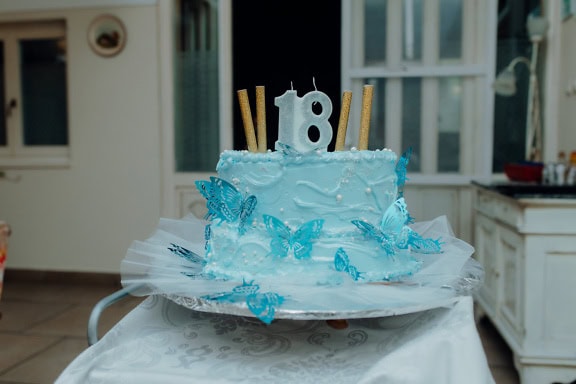 Gâteau d’anniversaire bleu avec bougie en forme de numéro dix-huit (18) et avec des papillons et du glaçage sur le dessus