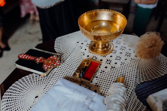 Tigela de ouro em uma mesa ao lado de uma bíblia com cruz e outros objetos religiosos usados durante a cerimônia de batismo