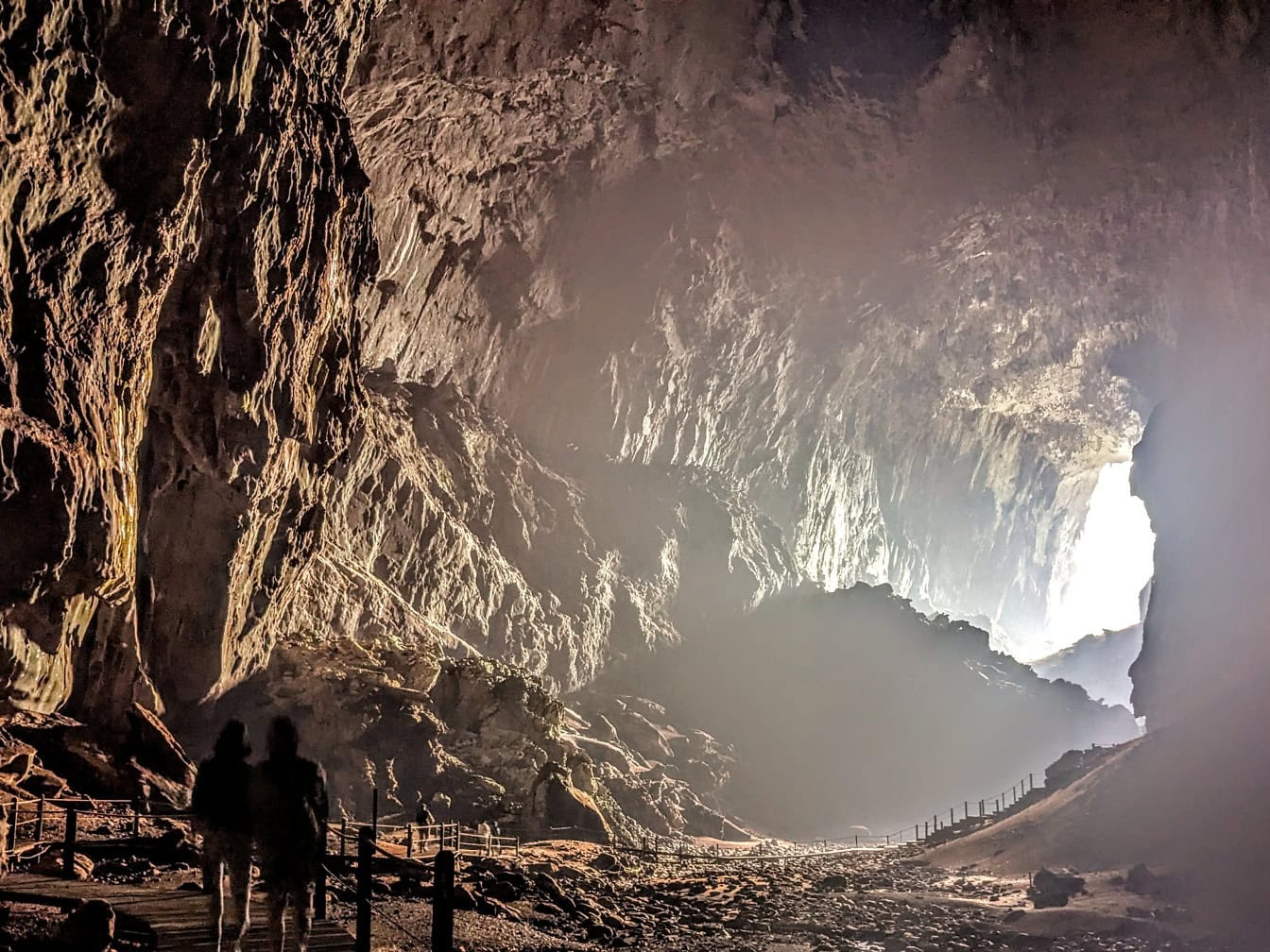 Siluetas de personas explorando una cueva subterránea con luz al final del túnel de la cueva en la cueva del ciervo en Borneo, Malasia