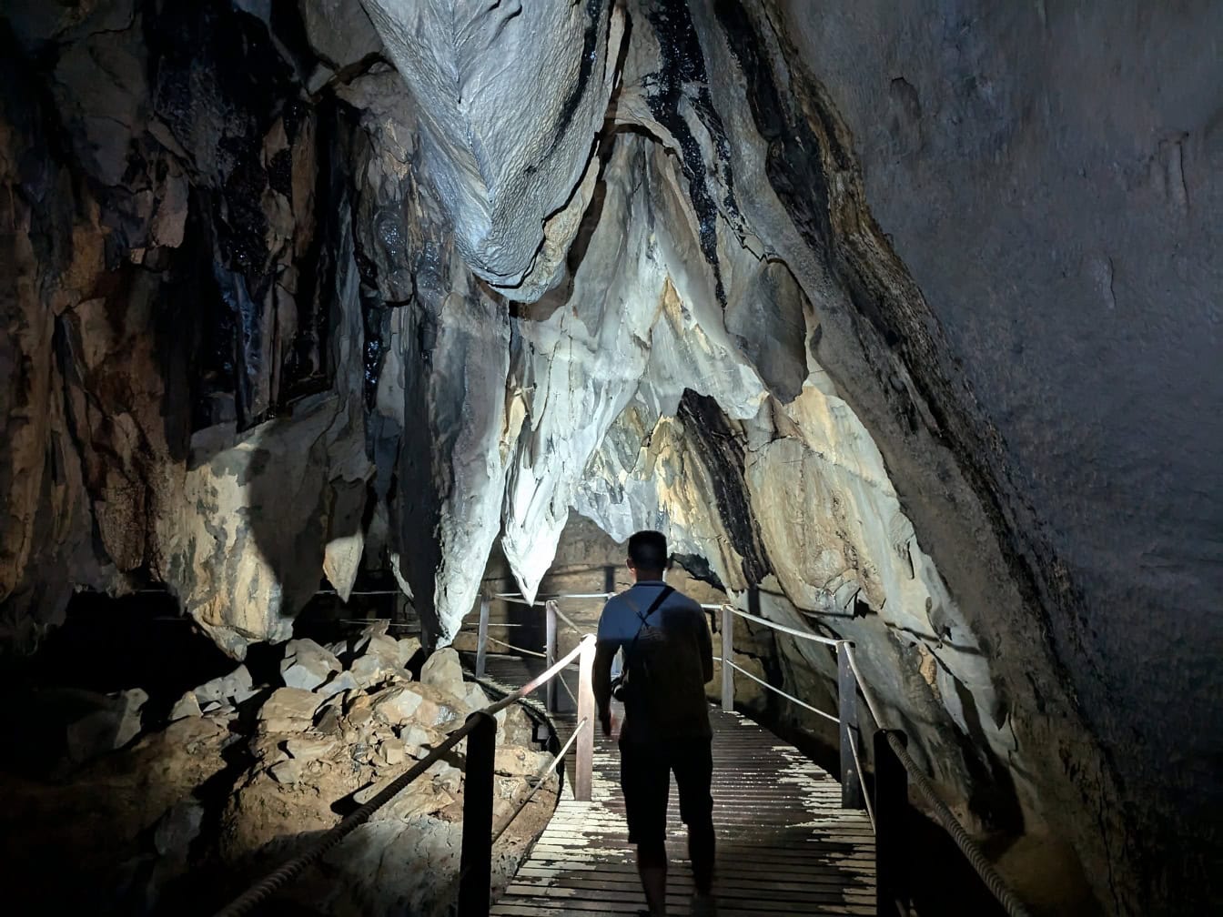 Homem andando na ponte de pedestres na escuridão de uma caverna Racer no parque nacional Mulu, Sarawak, Malásia