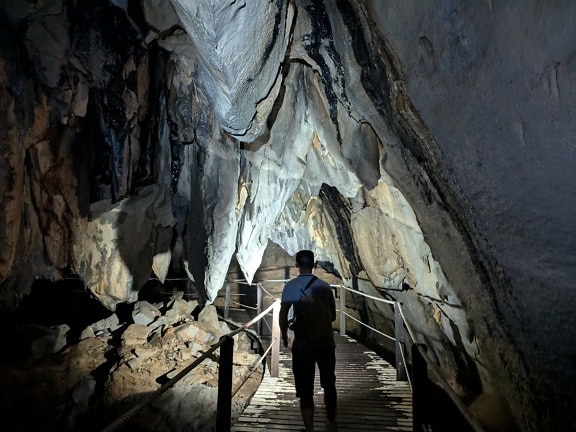 Mand går på fodgængerbro i et mørke i en Racer-hule i Mulu nationalpark, Sarawak, Malaysia