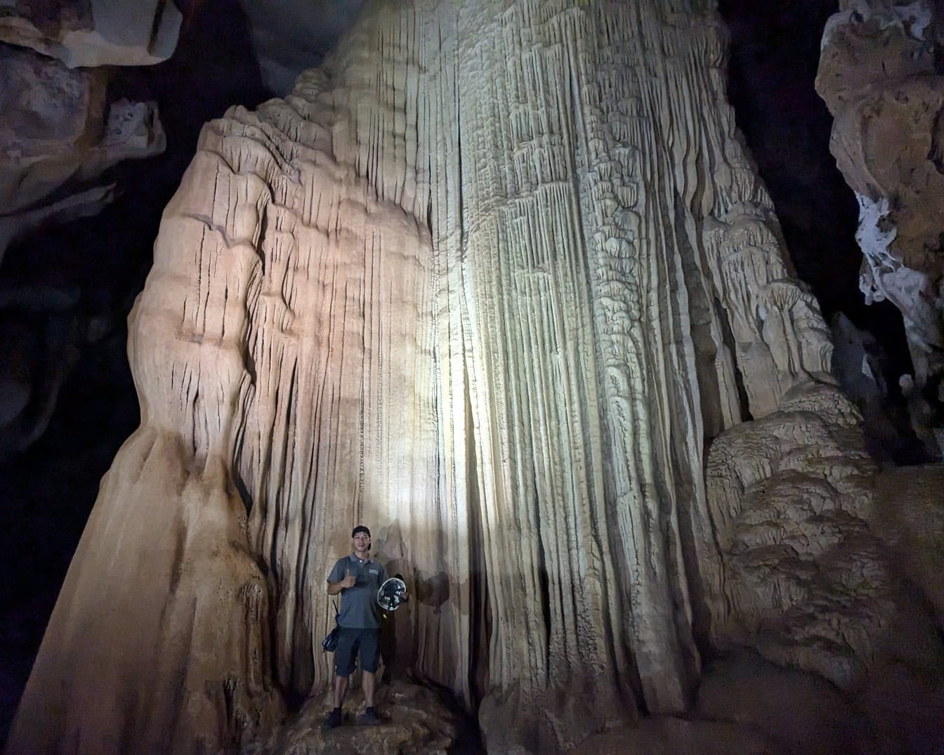 En spelunker, en som står i en underjordisk hule foran en enorm stalaktitt