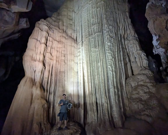 Een speleologie, een grotverkenner die zich in een ondergrondse grot voor een enorme stalactiet bevindt