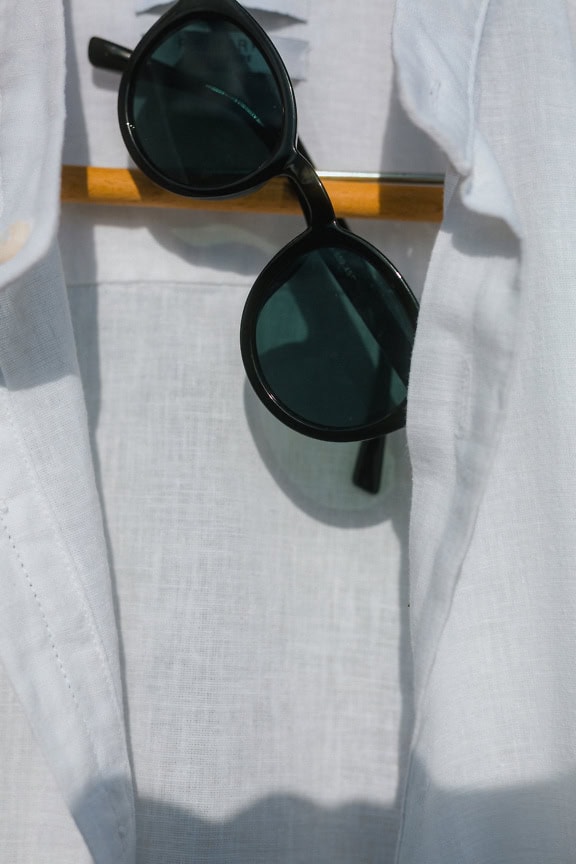 Des lunettes de soleil noires rétro et une chemise blanche classique sur un portemanteau