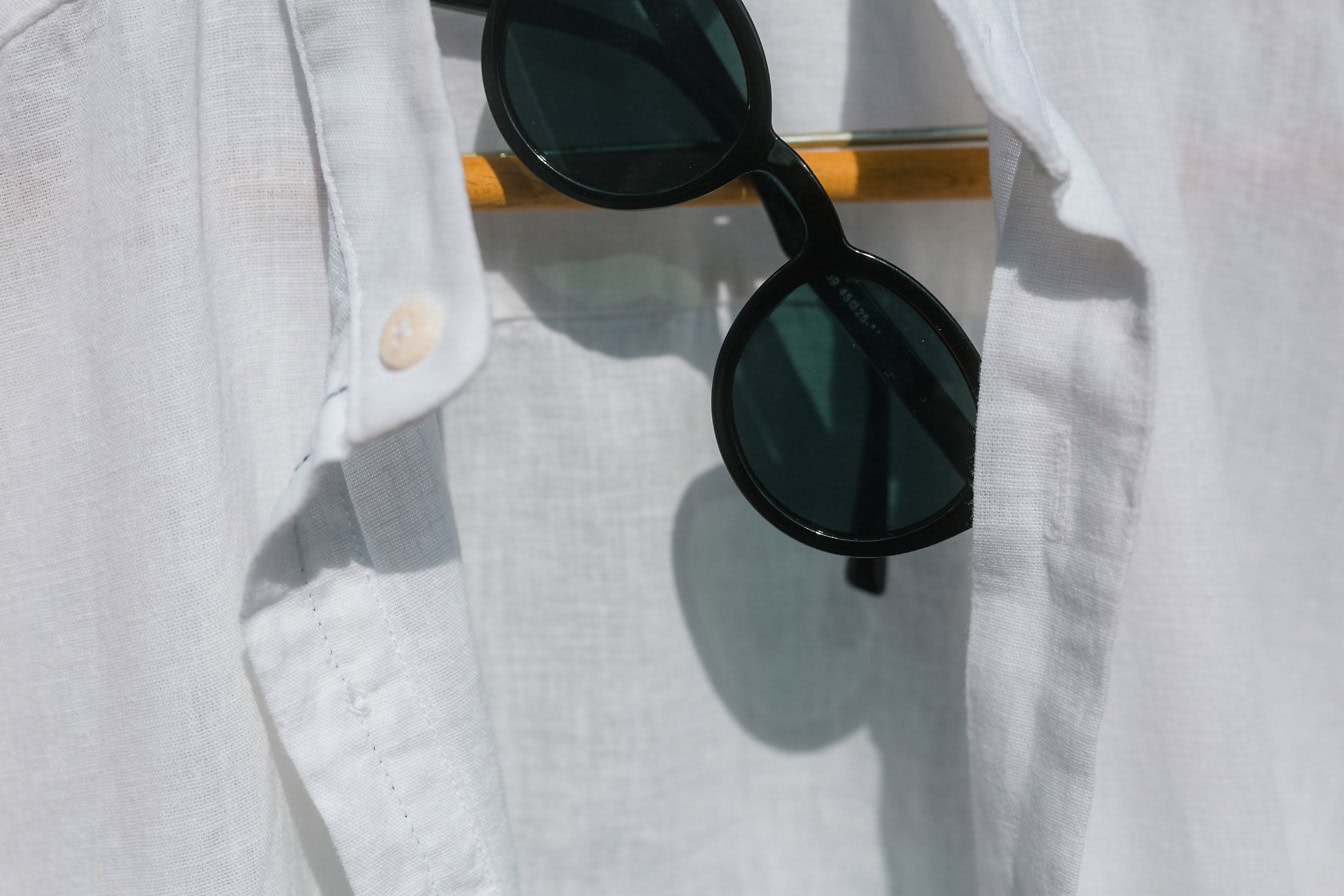 Des lunettes de soleil noires classiques et une chemise blanche sur un doigt