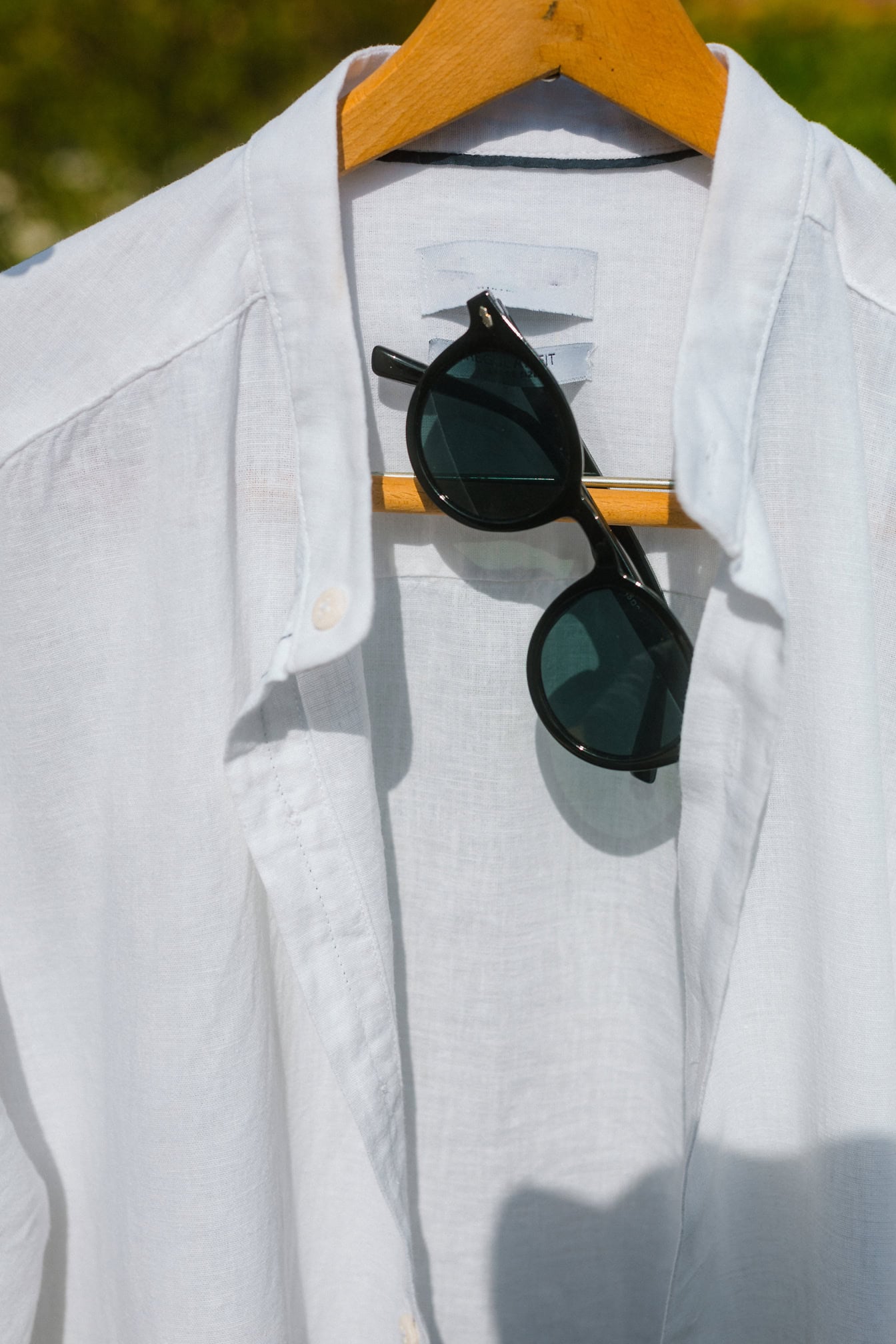 Camisa branca com óculos de sol pretos pendurados em um cabide de madeira