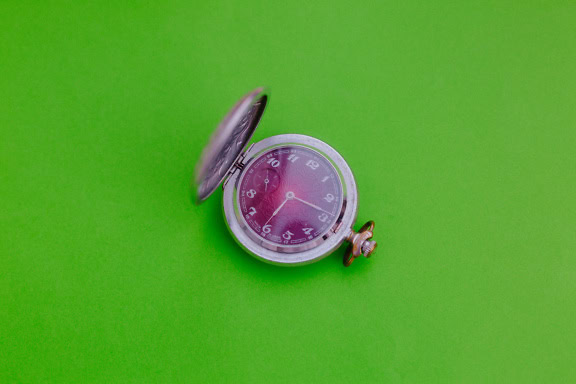 Oldfashined analog clock, a traditional pocket watch on a green surface