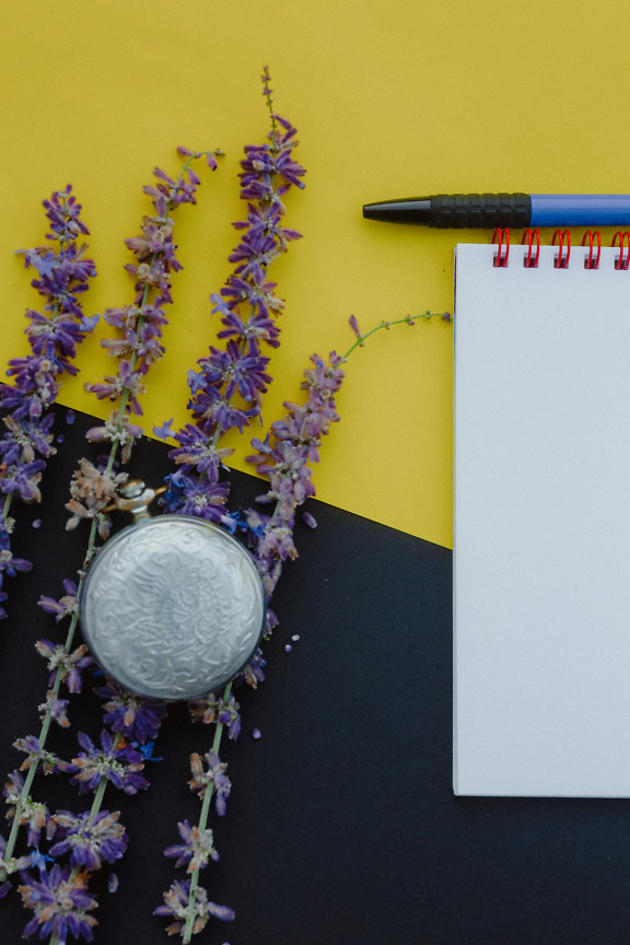 Notesbog og kuglepen ved siden af lavendelblomster og gammelt lommeur