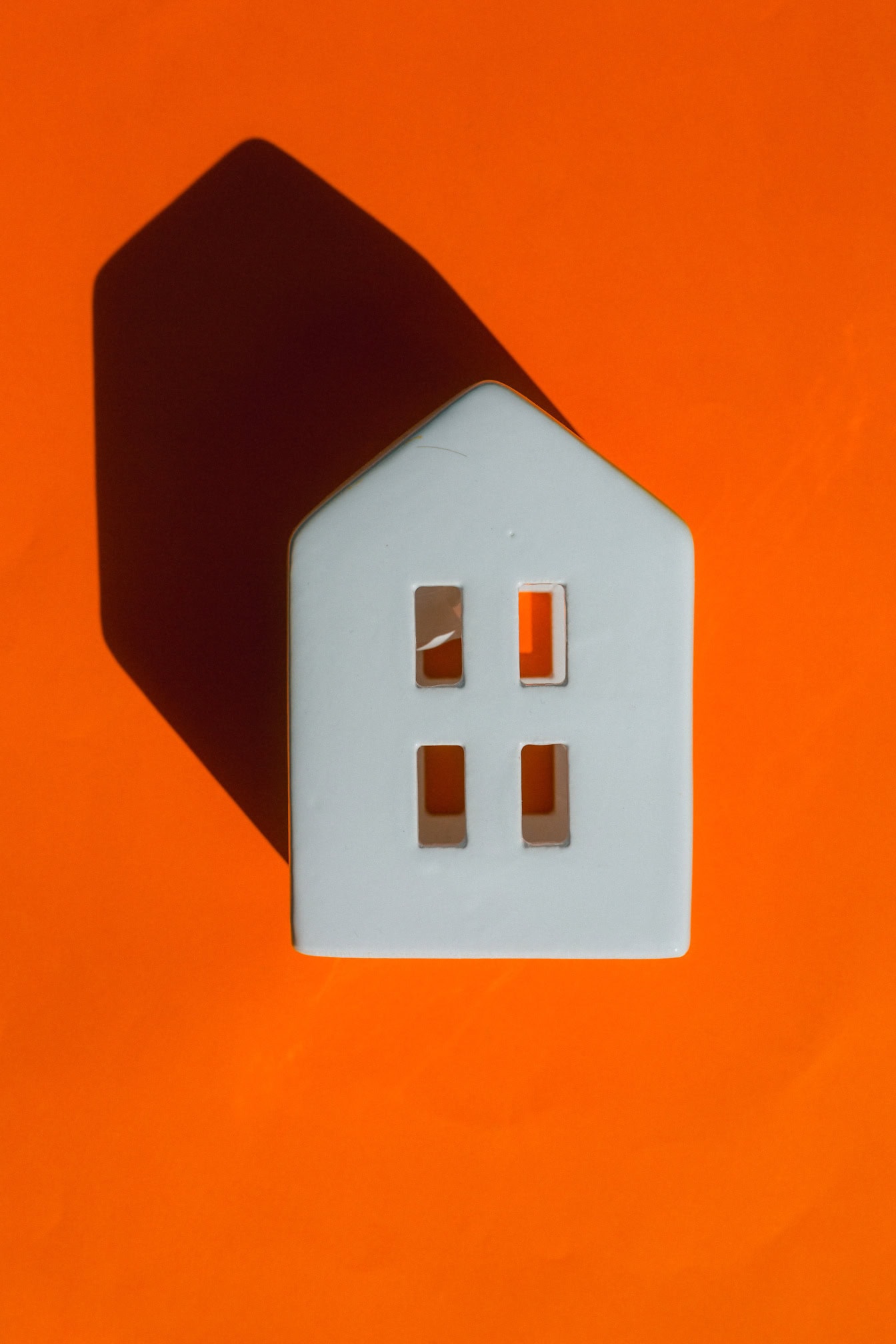 Small porcelain white house with long shadow on an orange background