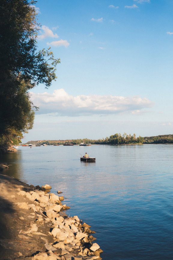 A fisherman in a boat on the Danube with a river port in the background