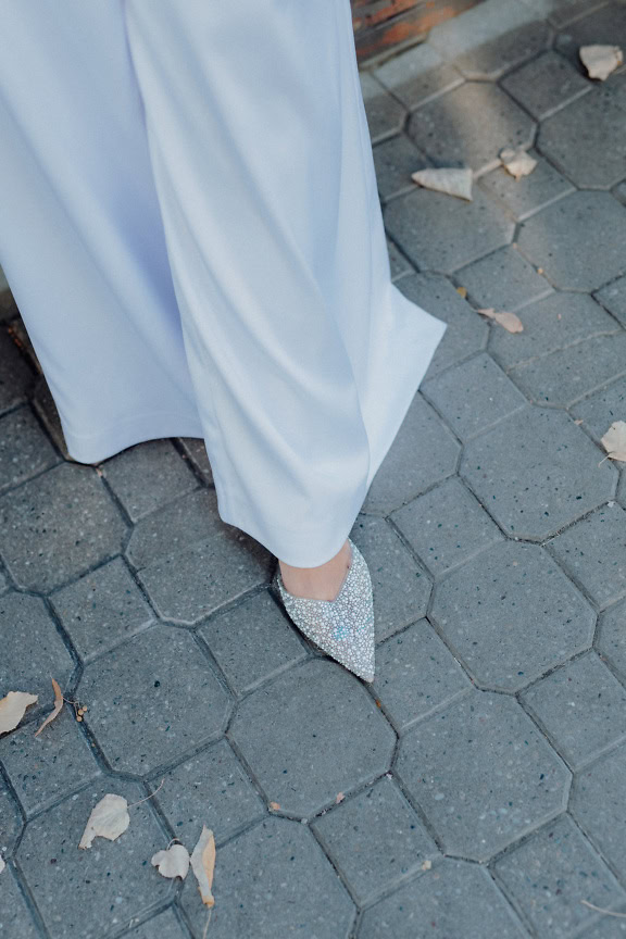 Person wearing white elegant pants and a sparkly elegant shoe with zircon decorations