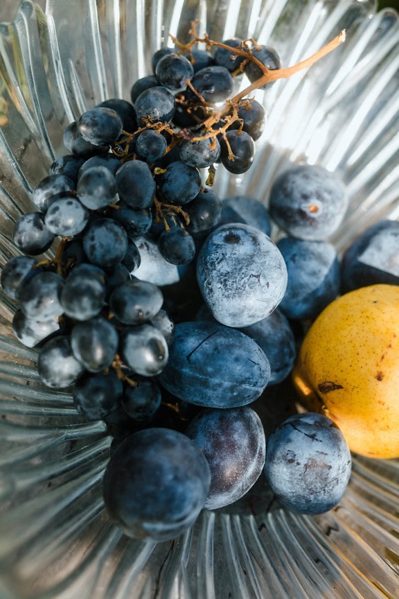 Una ciotola di vetro con frutta biologica, uva, prugna blu e pera