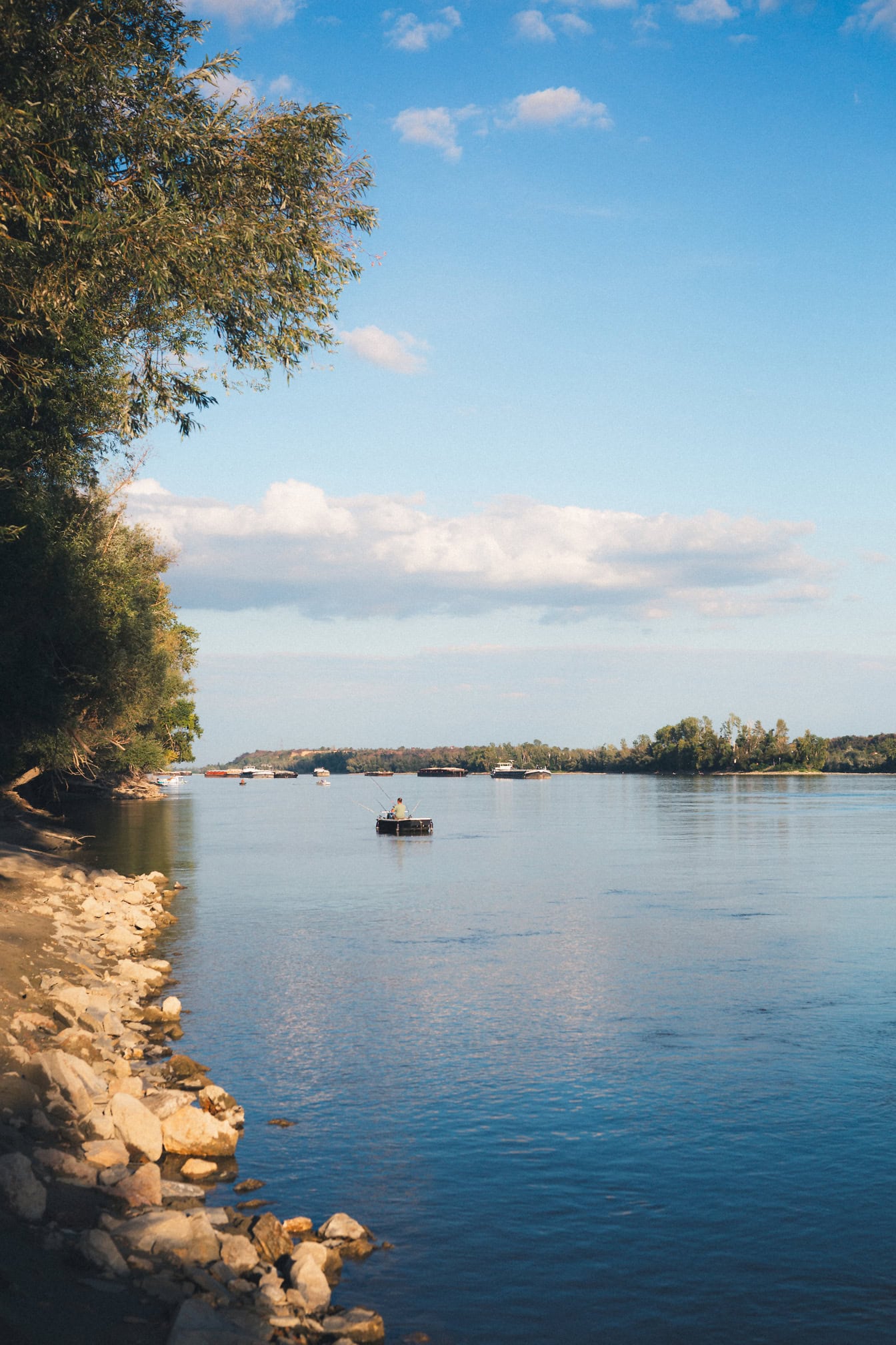 En steinete elvebredd av Donau med fiskebåter i det fjerne