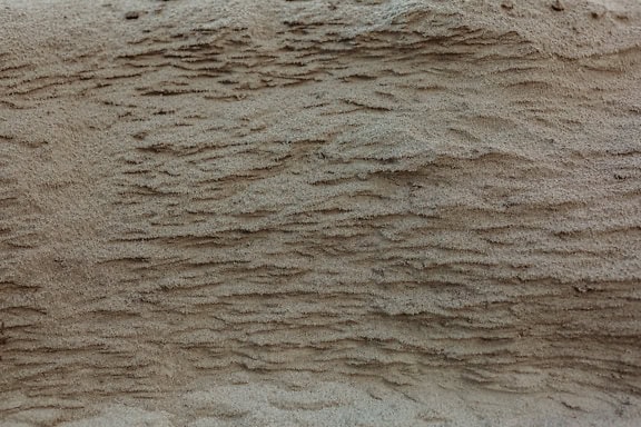 Nahaufnahme von halbnassem Sand, rauer Textur von hellbraunem Sandboden