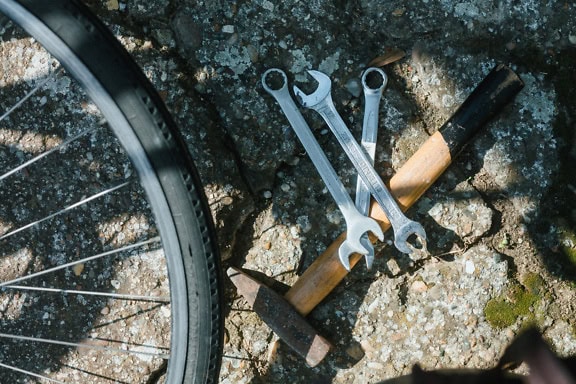 Hammer and mechanic’s chrome-vanadium wrenches on concrete next to wheel, hand tool for bicycle repair