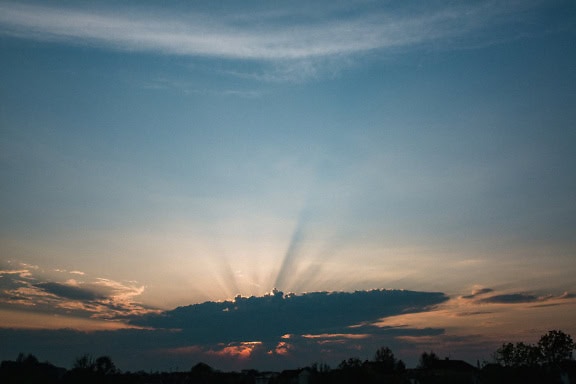 Auringonsäteitä sinisellä taivaalla harmaiden pilvien takana aamunkoitteessa