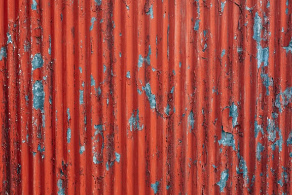 Galvanized metal sheet with corrugated surface with dark red paint peeling off from it