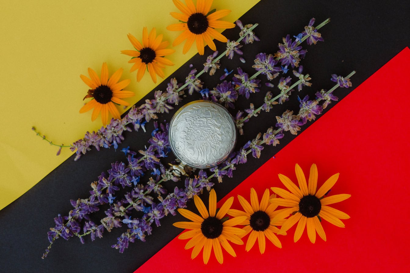 Montre de poche en argent avec fleurs oranges et lavande sur surface jaune, noire et rouge foncé