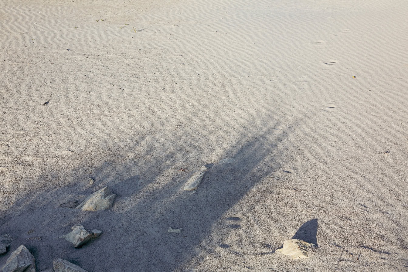 Helder grijs zand met rotsen en schaduwen op het strand