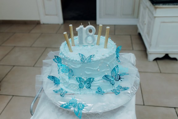 A birthday cake for celebration of an adulthood with a candle in a shape of number eighteen (18) and with butterflies and icing on top