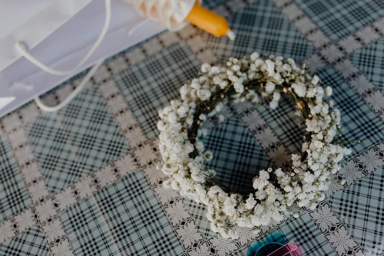 Krans med små vita blommor och ett ljus på en rutig duk