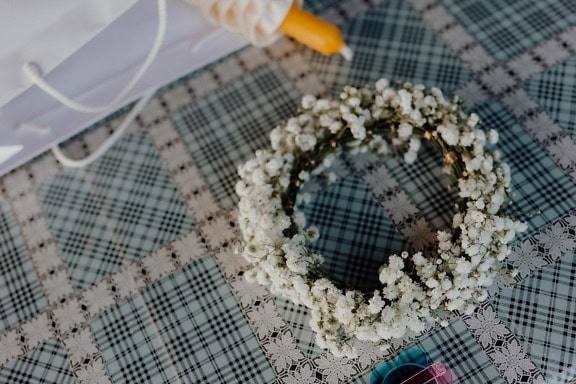 Wreath with small white flowers and a candle on a checkered tablecloth