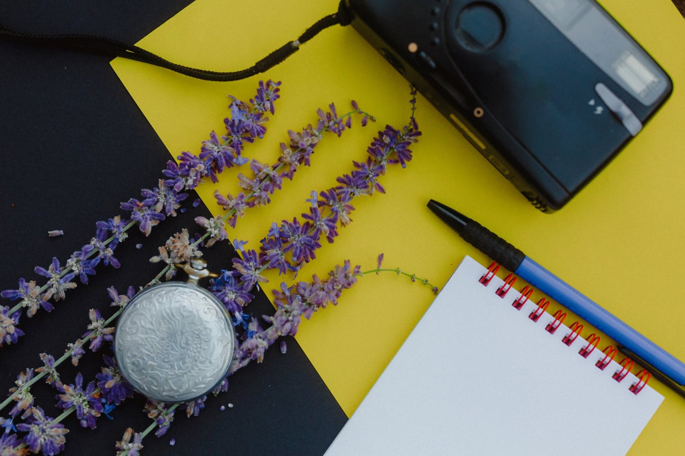 De pen van het blocnote en een zilveren zakhorloge met oude fotocamera op een gele en zwarte achtergrond