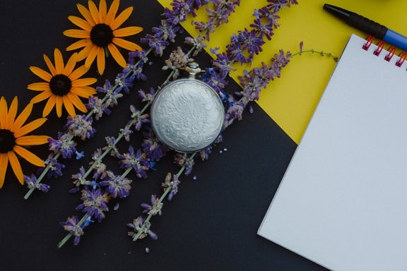 Reloj de bolsillo analógico plateado anticuado y flores sobre fondo negro y amarillo