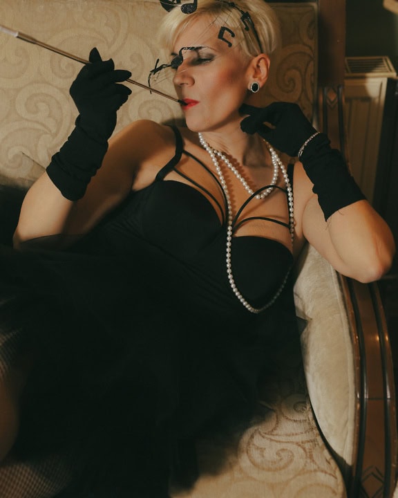 Woman in a black dress, gloves and glamour hat smoking a cigarette on a couch