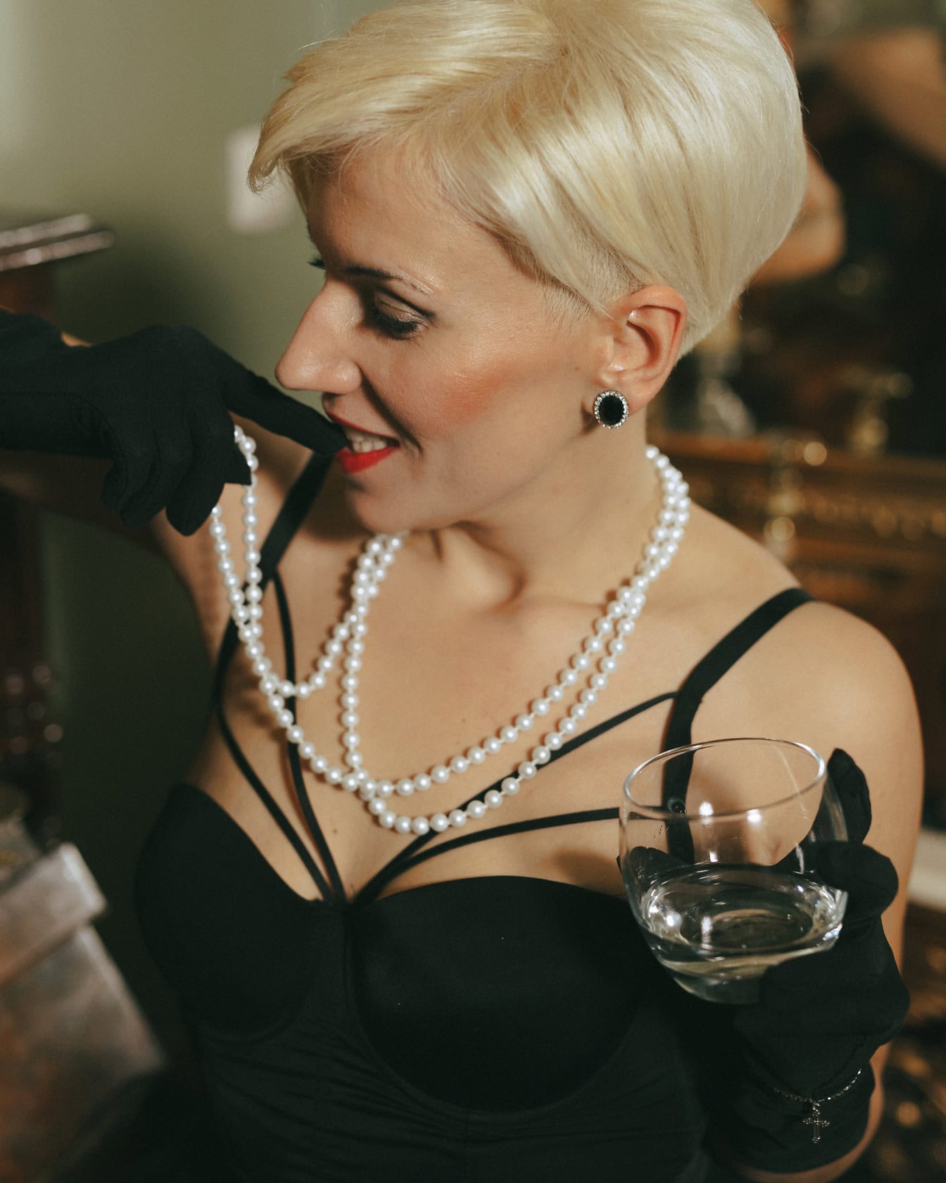 Portret van een glamourvrouw die een zwarte kleding en handschoenen draagt die een glas water houden