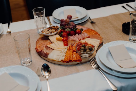 Plate of slices of ham and sausage with fresh fruits and other appetizer food on a table