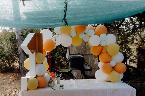 Dekoration för 1-årsfest med orange-gula och vita ballonger och med dekoration i form av nummer ett (1)