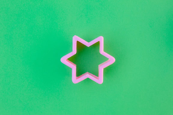 Cortador de galletas rosa de plástico en forma de estrella sobre fondo verde