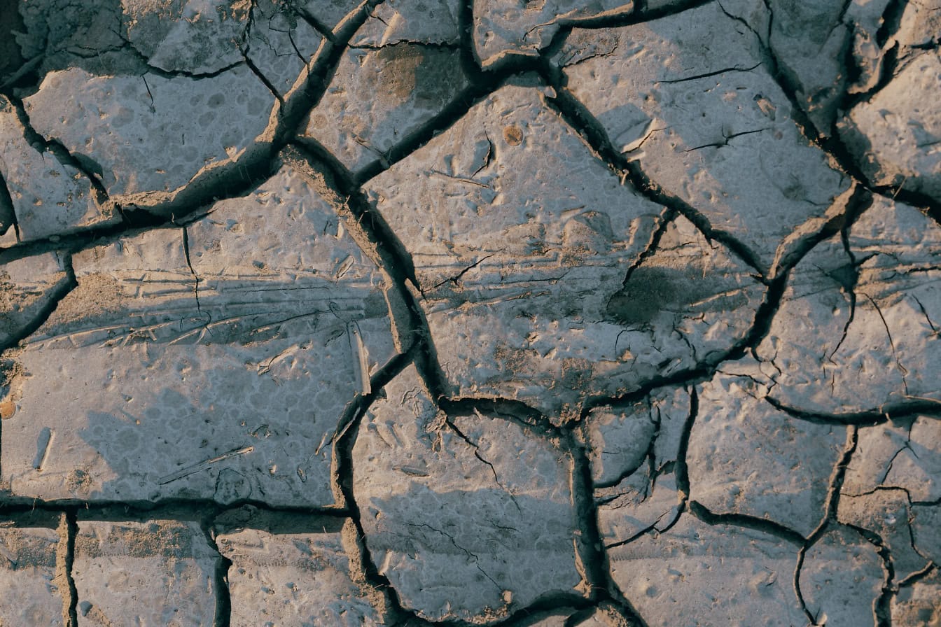 Nahaufnahme eines trockenen, rissigen Bodens, eine Textur aus ausgetrocknetem Schlamm während der Dürre