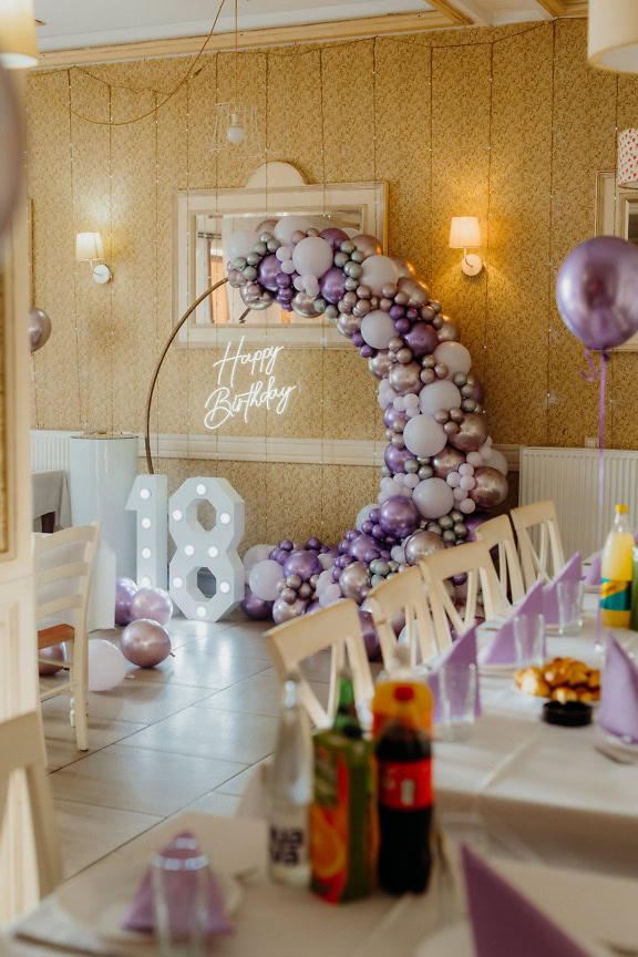 Quarto decorado para festa de aniversário com balões brancos e arroxeados e um sinal de néon iluminado do feliz aniversario