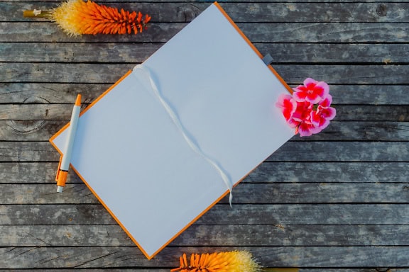 Opened notepad with blank white papers, a pencil and flowers on a wood table