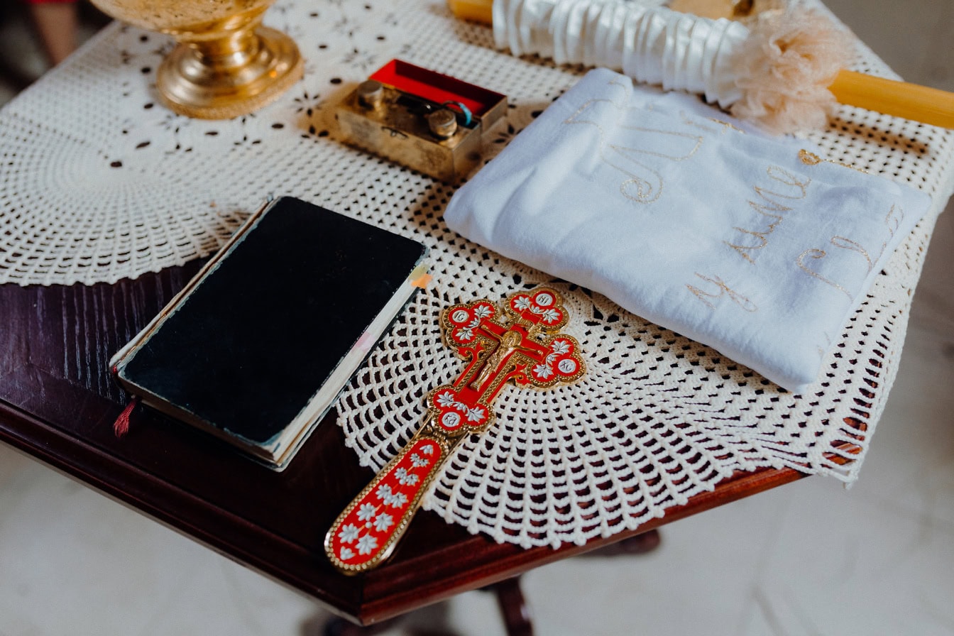 Un libro negro, una biblia de acebo y una cruz cristiana dorada con velas sobre una mesa, una reliquia en uso durante la ceremonia del bautismo