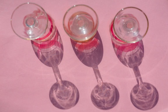 Row of crystal wine glasses with long shadow on pink surface