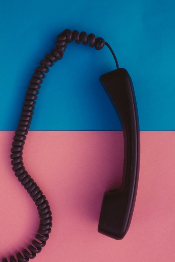 Handset met spiraalvormige kabel van een oude analoge telefoonontvanger op een blauwe en roze achtergrond