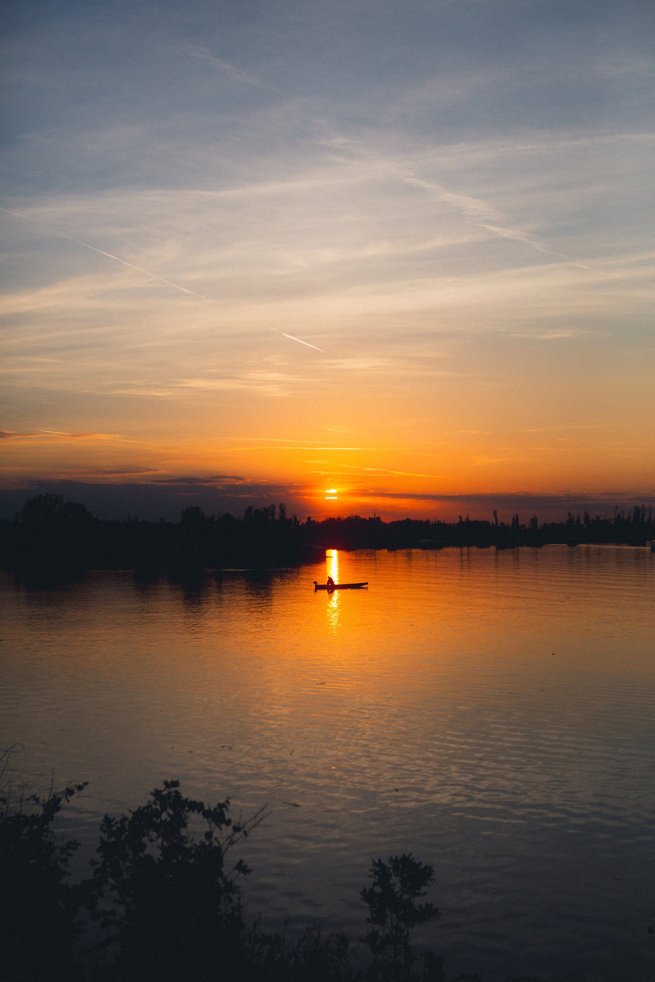 Person i en båd på en Tikvara-sø ved siden af en Donau-flod under solnedgang