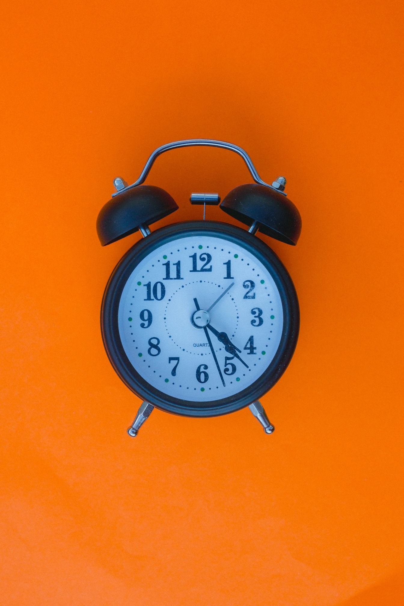 Old black analogue alarm clock with bells on an orange background