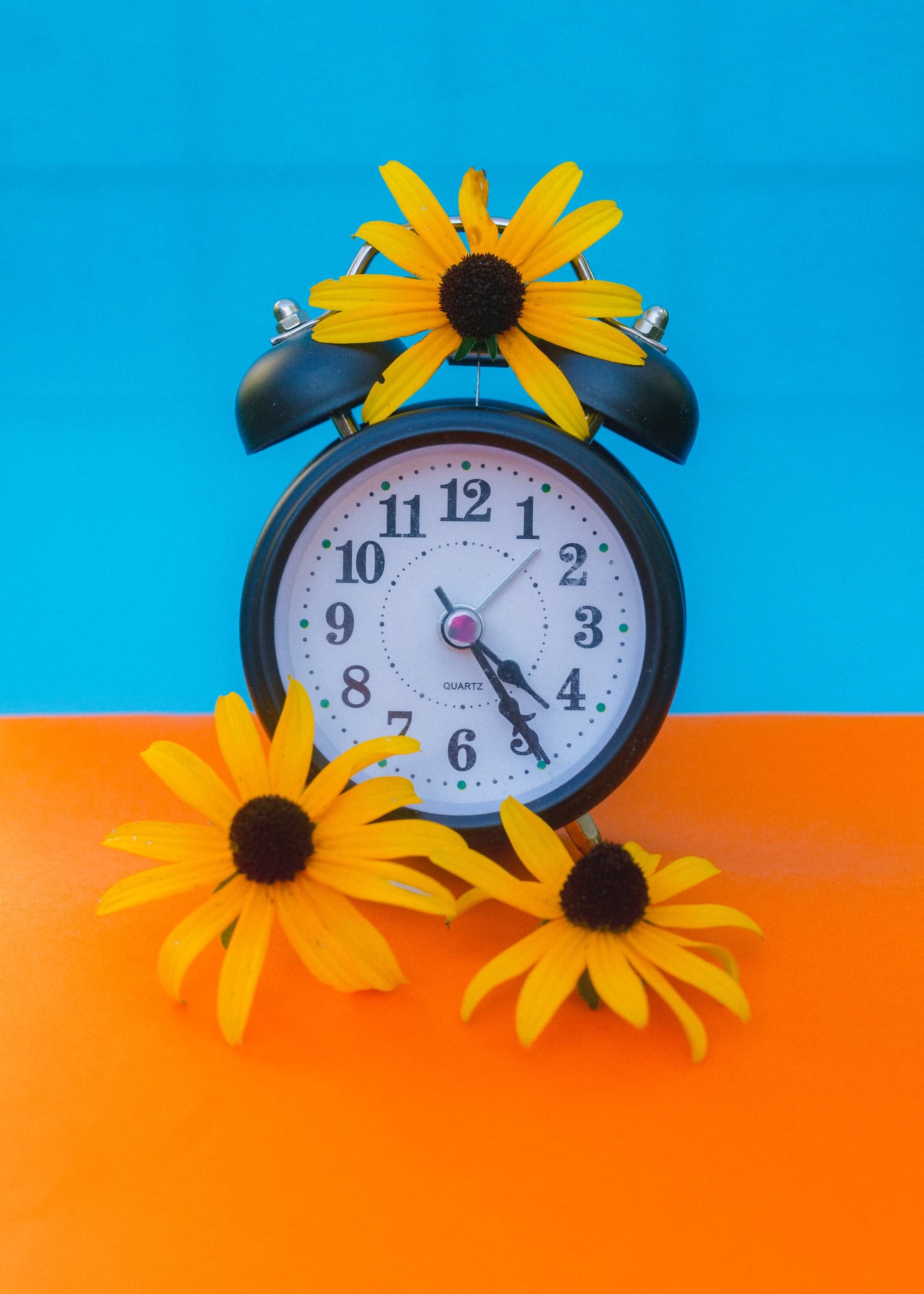 Een oude analoge wekker met bloemen op blauwe en oranje achtergrond