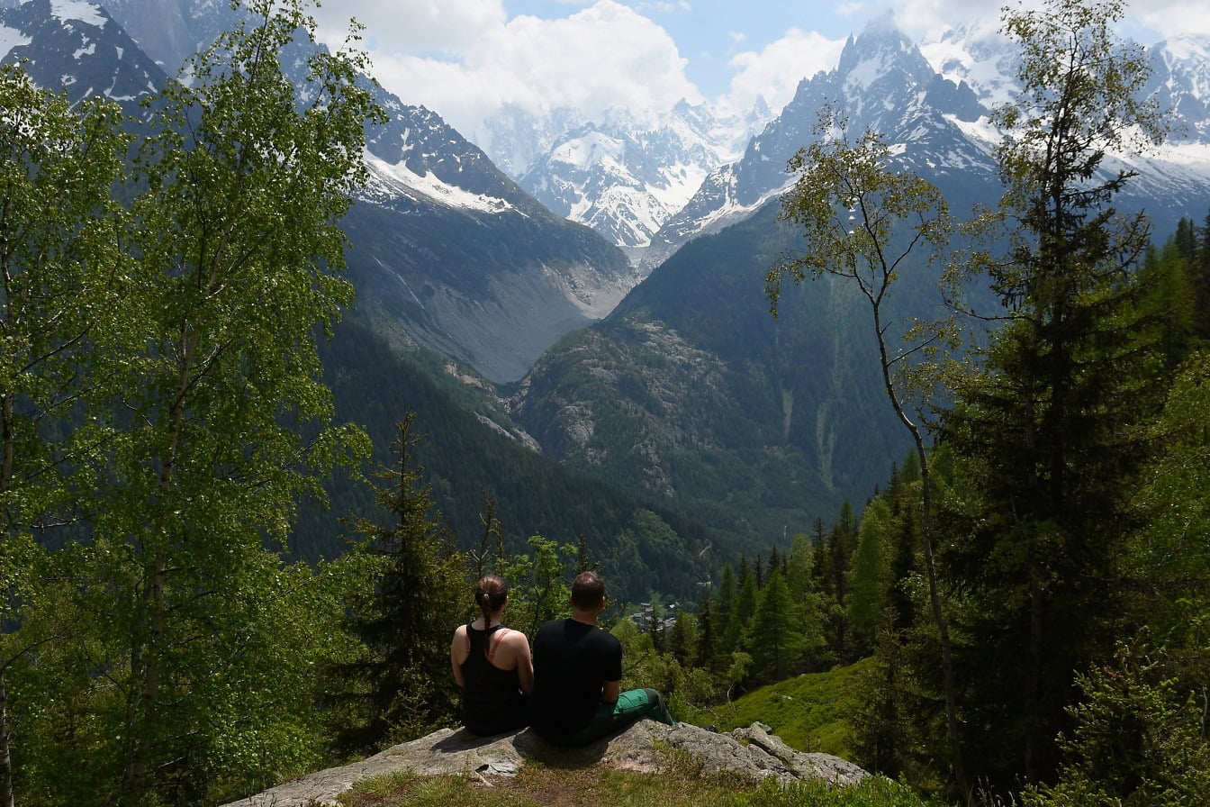 Mann und Frau sitzen auf einem Felsen und blicken auf Berge