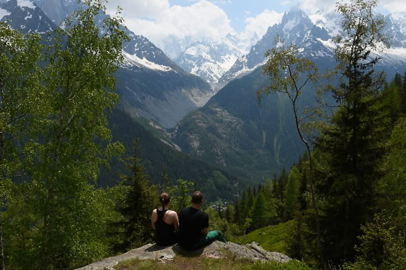 Mand og kvinde sidder på en klippe og kigger på bjerge