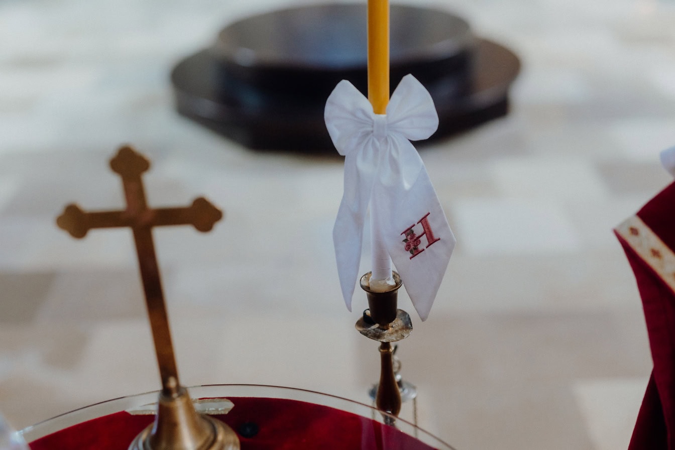 Una vela con una pajarita blanca decorativa sobre un candelabro, reliquias para la ceremonia del bautizo