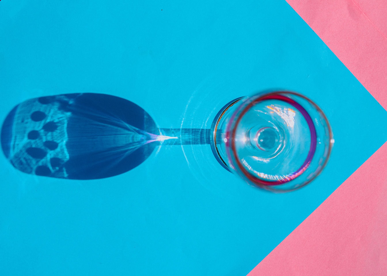 Shining crystal wine glass with a long shadow on a blue and pink surface