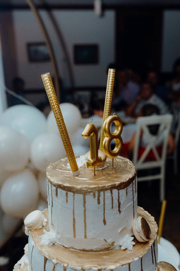 Pastel con glaseado de oro y velas en la parte superior en la fiesta de cumpleaños para celebrar el decimoctavo cumpleaños