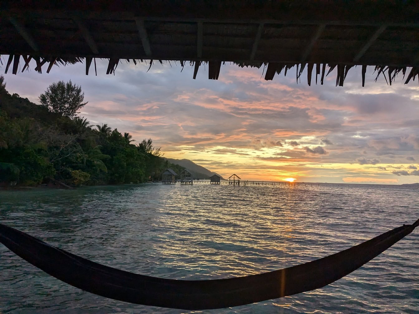 Tempat tidur gantung di atas air dengan matahari terbenam di atas teluk di laguna