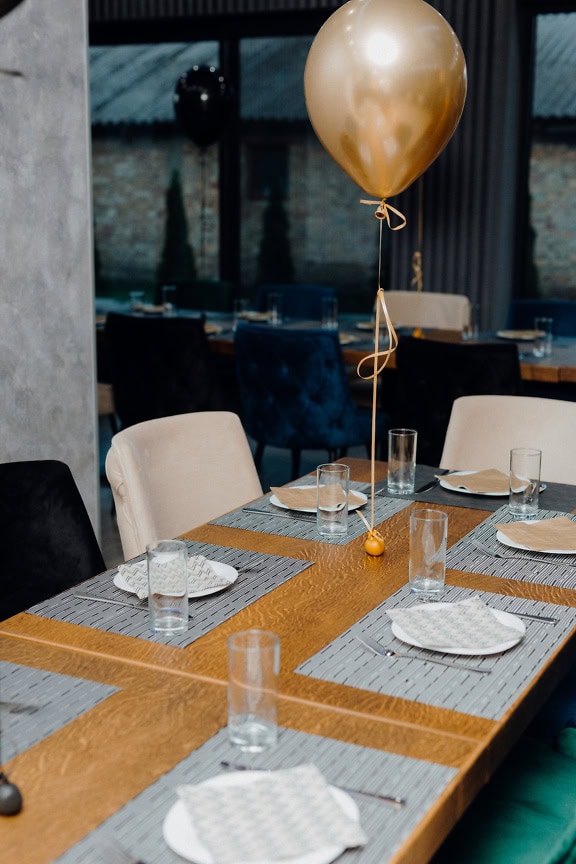 Dining table set for celebration dinner with plates and glasses and a balloon