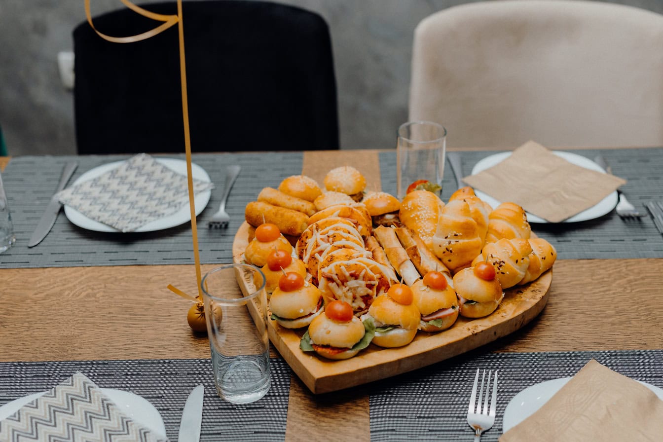 A hart shaped tray of miniature burgers and sandwiches as appetizer food on a table